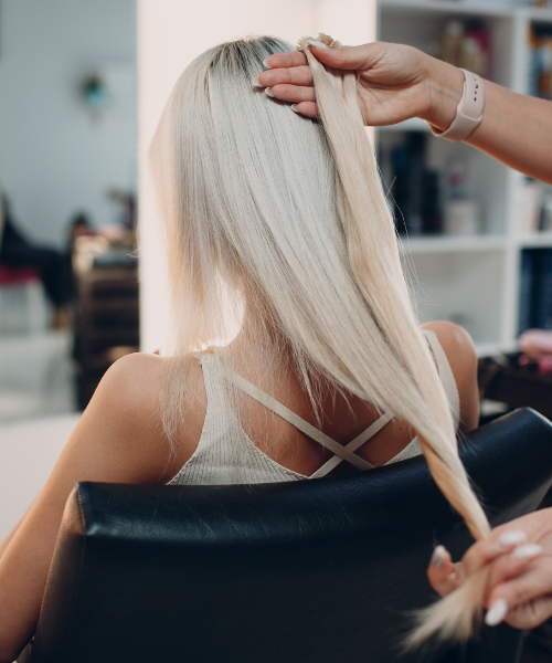 Hairstylist checking long, straight platinum blonde hair in salon