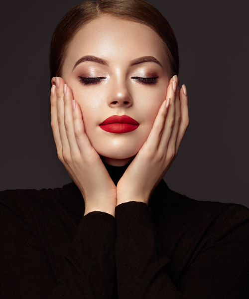 Elegant woman with red lips touching cheeks, eyes closed in black backdrop