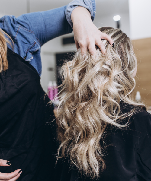 Hairstylist styling wavy blonde hair with hand in hair salon