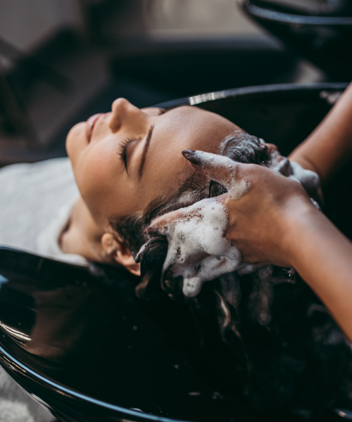 Hair washing at salon, hands applying shampoo to client's wet hair